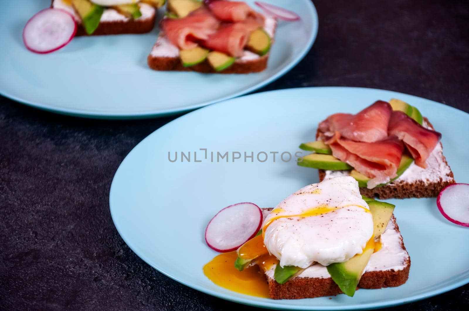 Bread Toasts with Cream Cheese, Avocado, Poached Egg and Salmon Fish on Dark Background. Healthy Breakfast or Appetizer Concept.