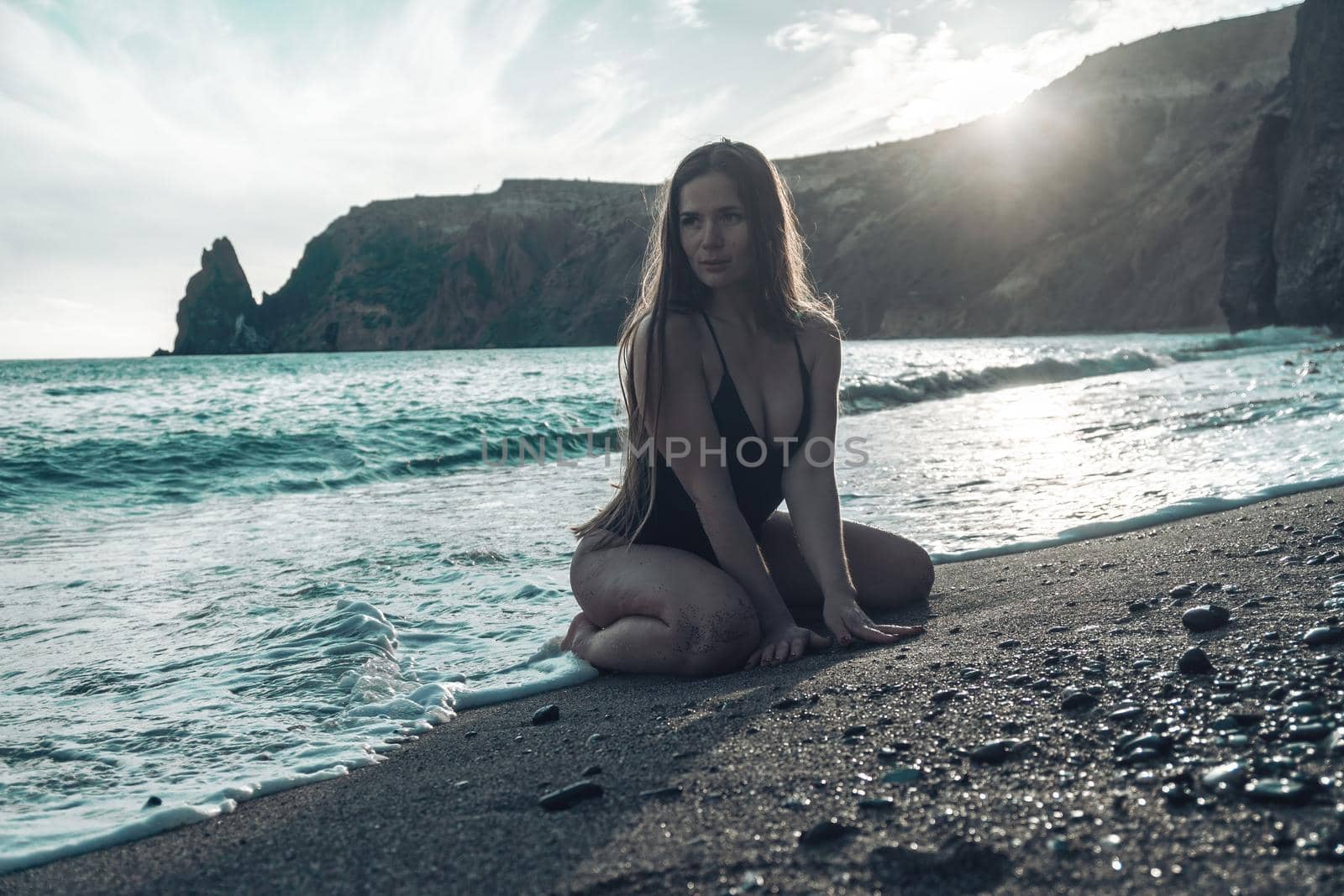 Selective focus. Happy carefree sensual woman with long hair in black swimwear posing at sunset beach. Silhouette of young beautiful playful positive woman outdoor. Summer vacation and trip concept by panophotograph