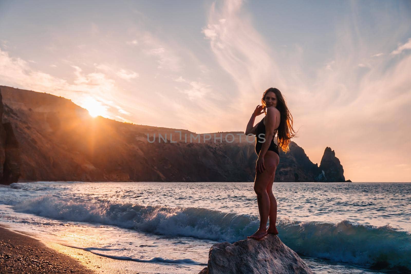 Selective focus. Happy carefree sensual woman with long hair in black swimwear posing at sunset beach. Silhouette of young beautiful playful positive woman outdoor. Summer vacation and trip concept by panophotograph