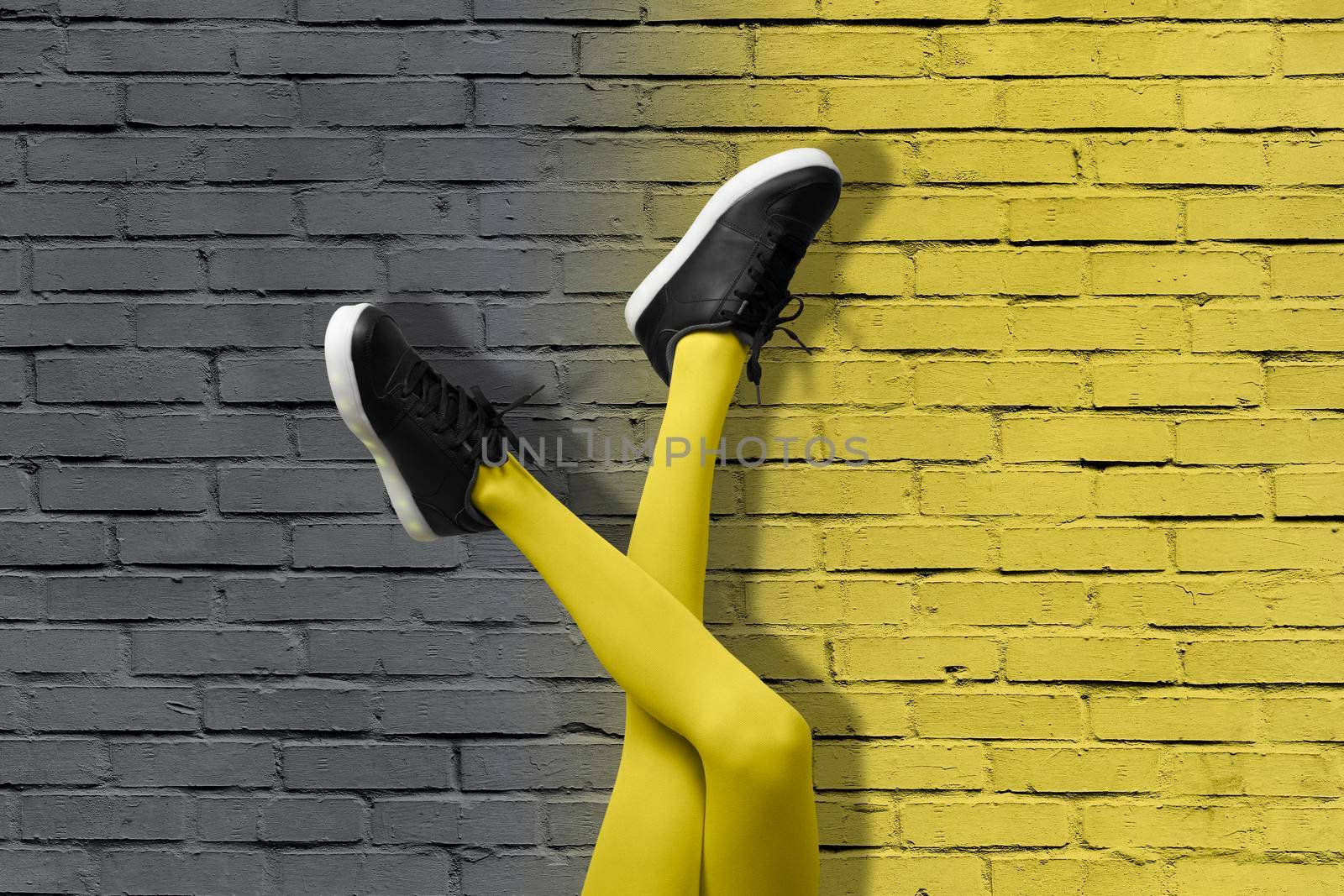 New Black female sneakers on long slender girl legs in yellow tights on background of gradient yellow and gray brick wall. Color of 2021 year pop art concept.