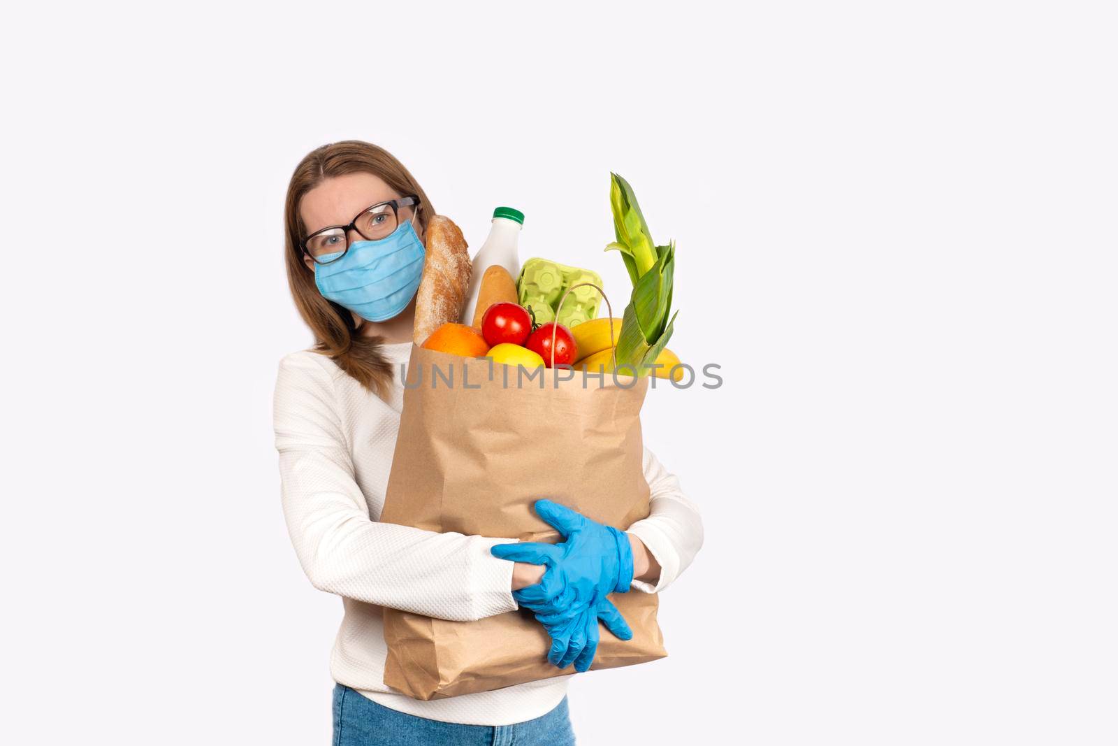 Safe food delivery or donation concept. Food delivery or shopping during coronavirus quarantine. Young woman in disposable gloves and face mask holding Box with food ingredients