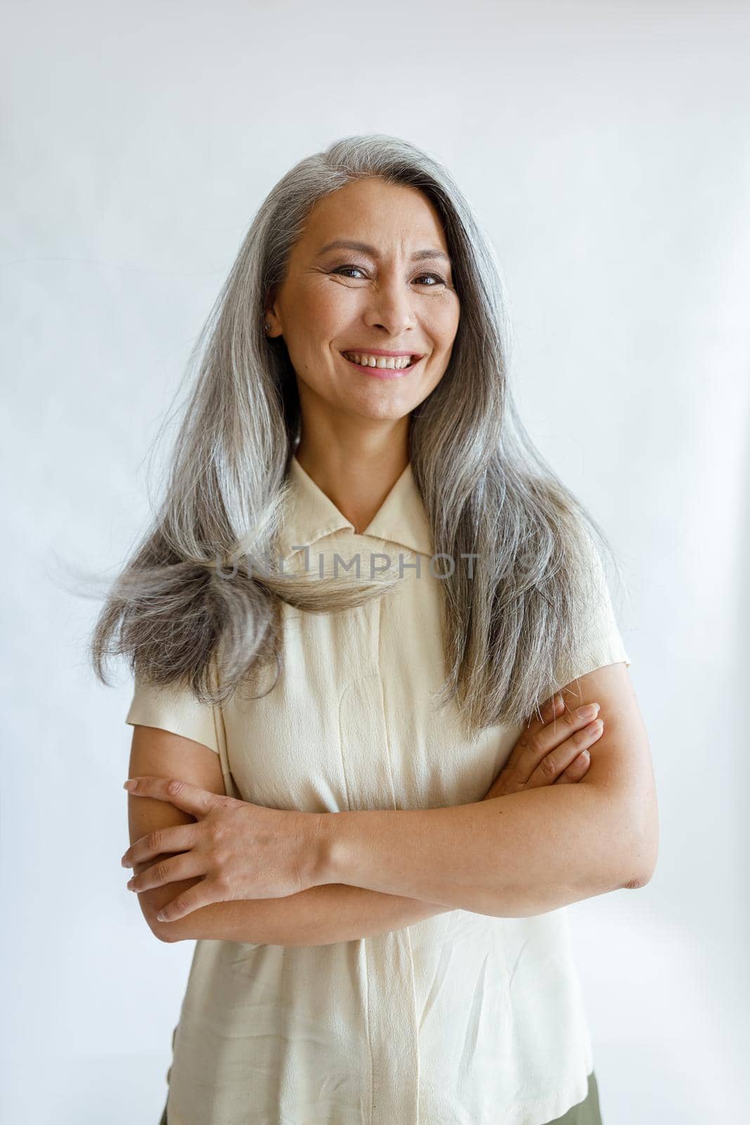 Portrait of Asian female model with long grey hair and crossed arms on light background by Yaroslav_astakhov