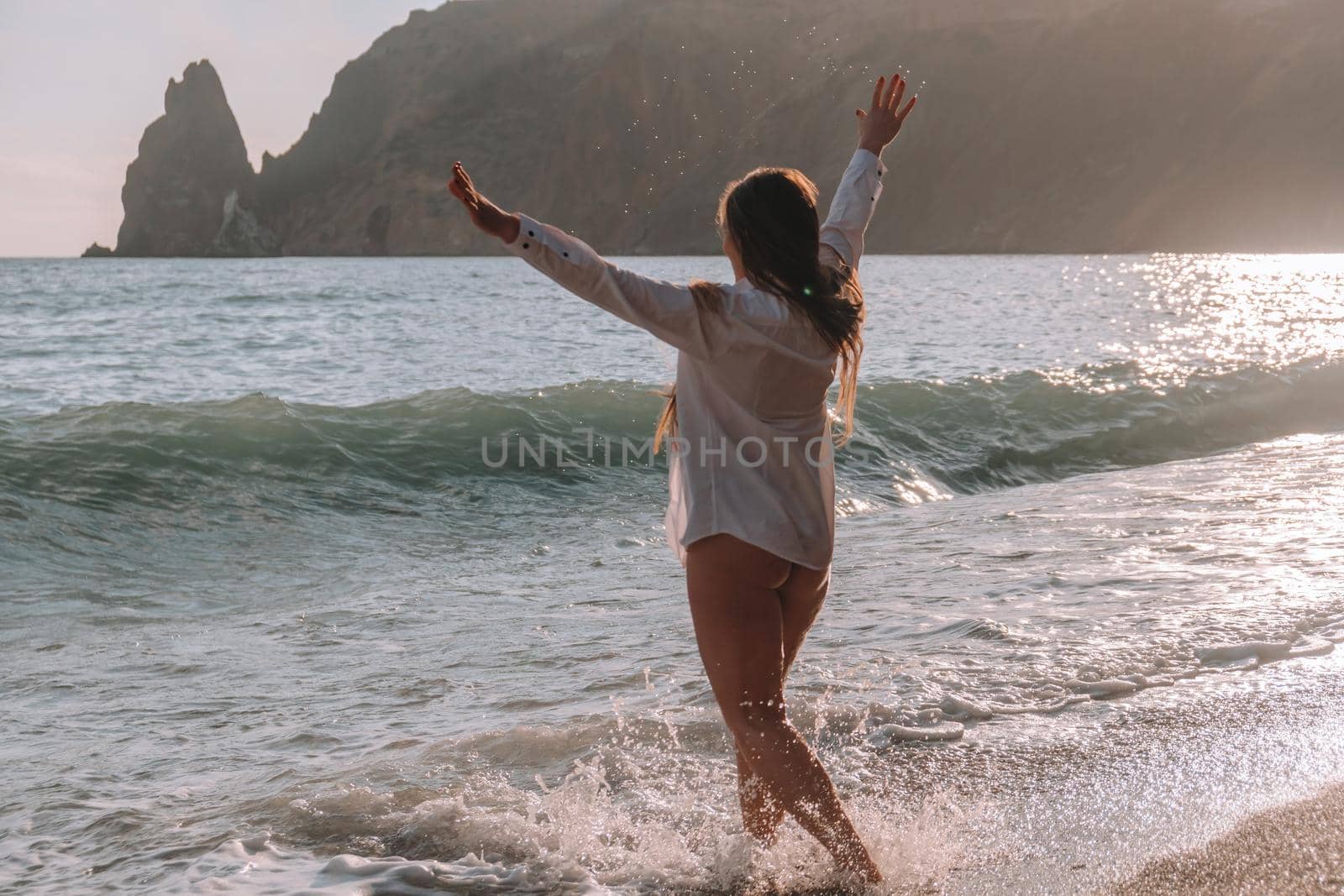 Selective focus. Happy carefree sensual woman with long hair in black swimwear posing at sunset beach. Silhouette of young beautiful playful positive woman outdoor. Summer vacation and trip concept.