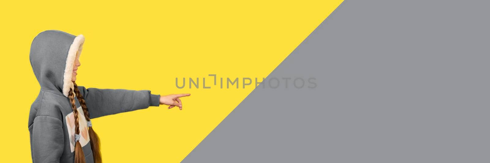 Teen beautiful girl in santa hat smiling and pointing her finger. Long horizontal Banner toned in trendy Ultimate Grey and Illuminating yellow colors of 2021.