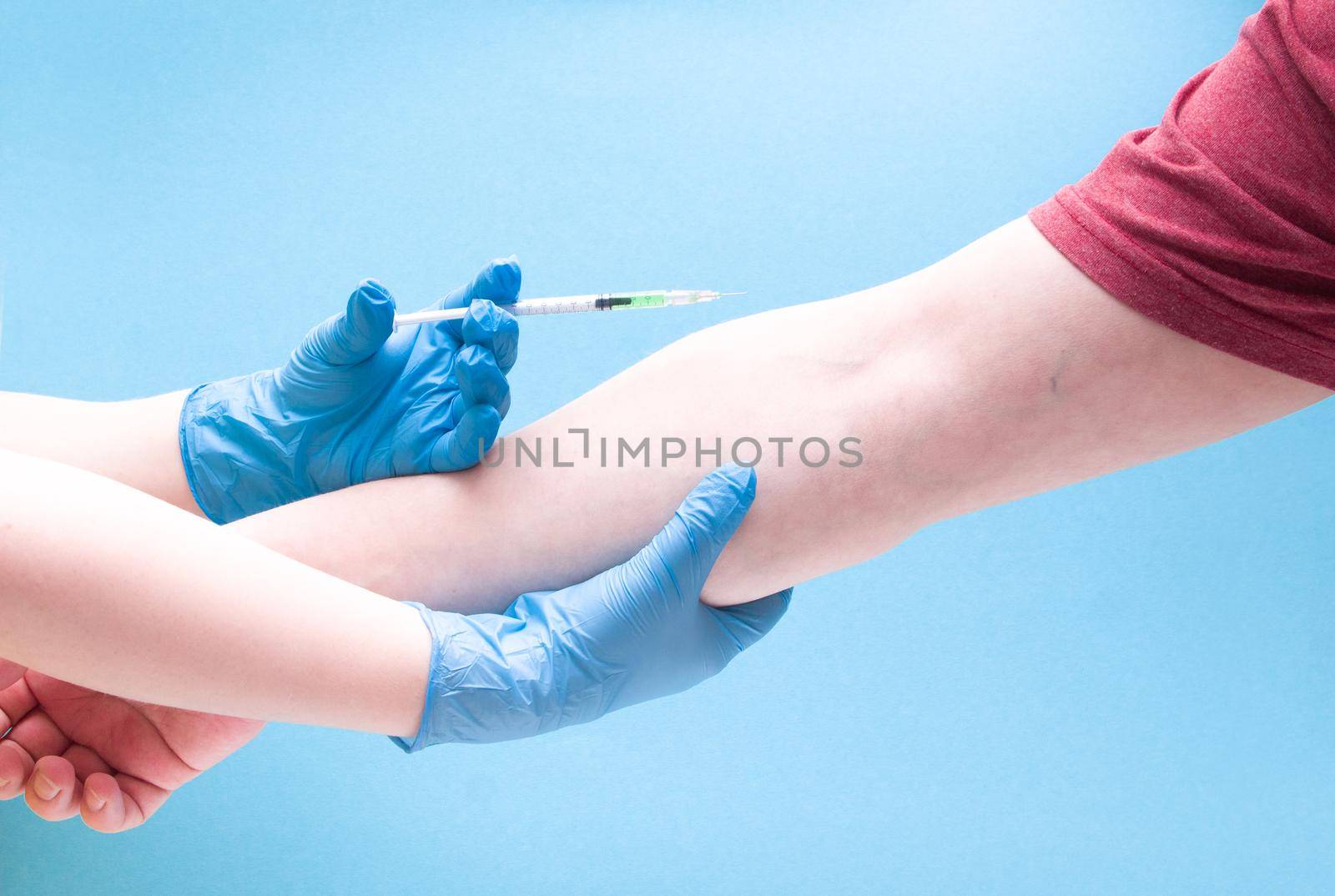 female hand in a blue rubber medical glove injects a male insulin syringe with a green vaccine on a blue background copy space, treatment and health care concept, stop coronavirus by natashko