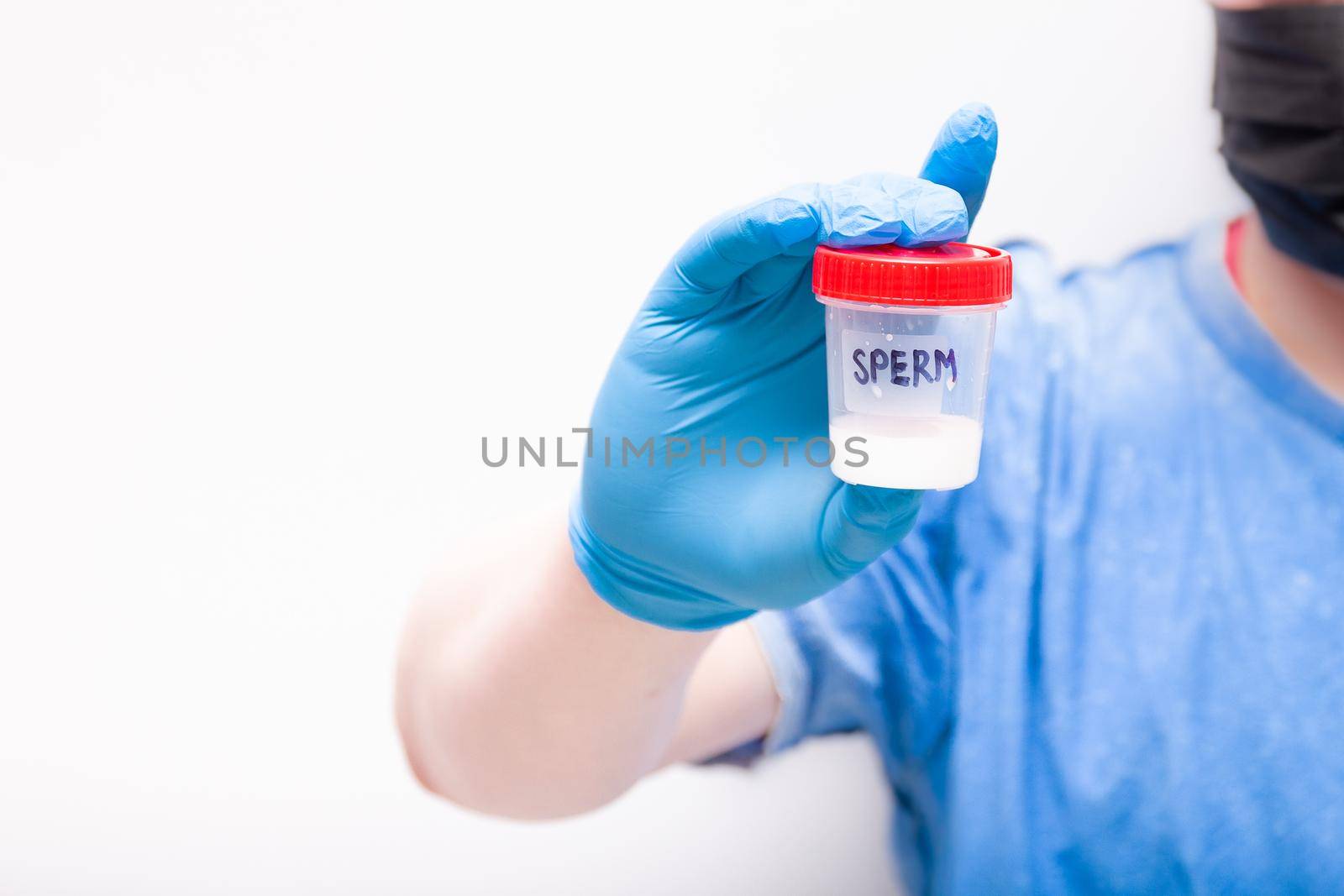 a man in goggles and a medical black mask holds a jar of sprerm in his hand. a hand in a blue disposable glove, a test jar with the inscription "sperm", blurred background, copy space