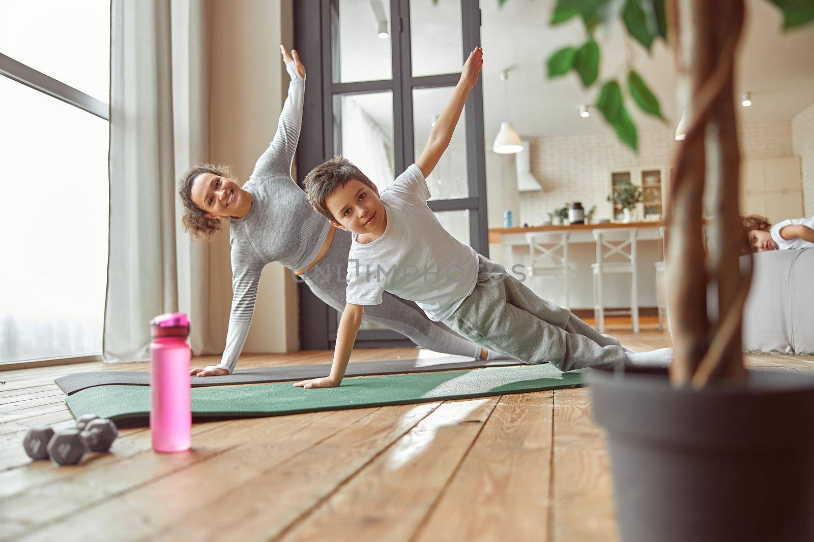 Full length portrait of happy woman doing side plank position with boy in living room