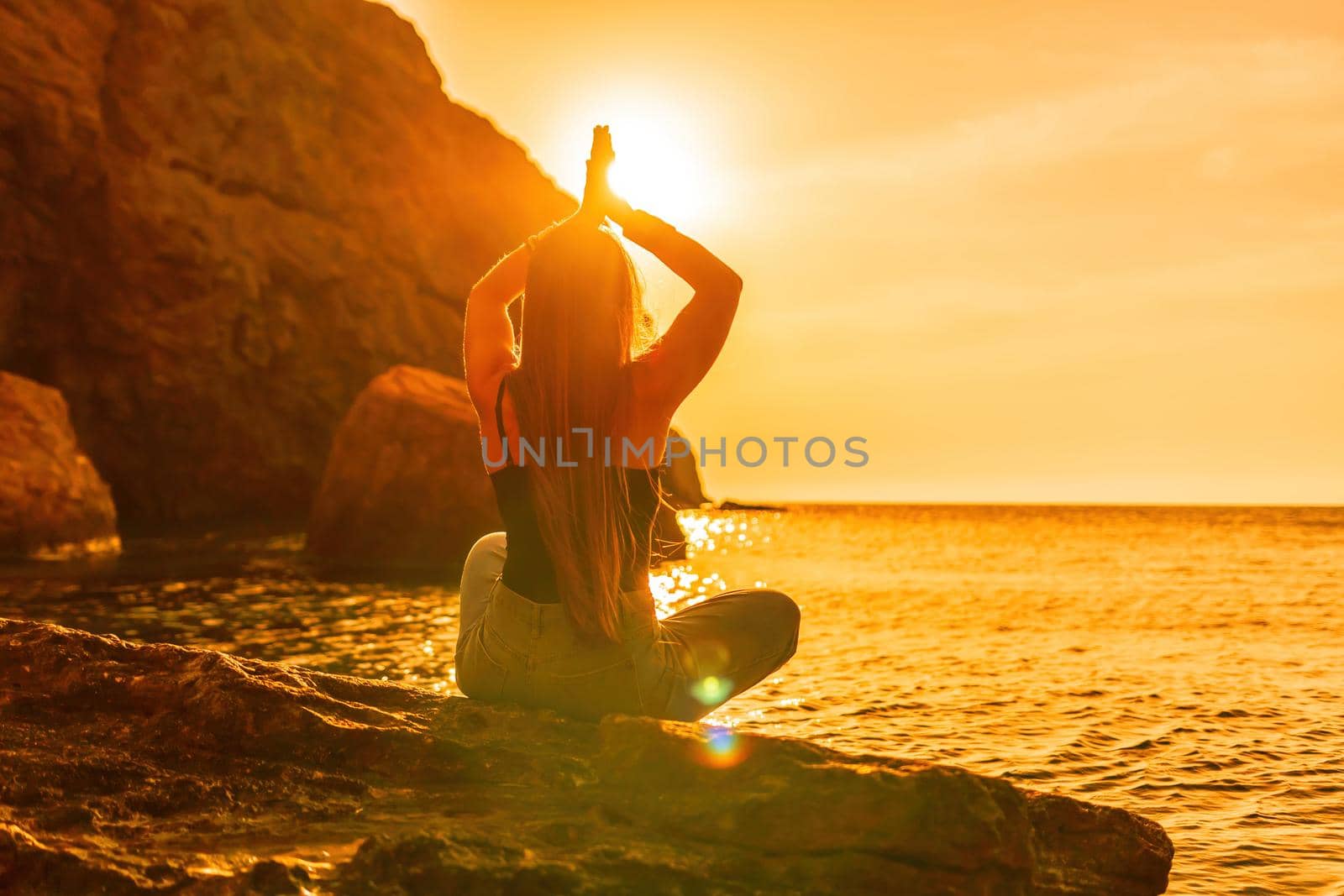 Young woman with long hair in black swimsuit and boho style braclets practicing outdoors on yoga mat by the sea on a sunset. Women's yoga fitness routine. Healthy lifestyle, harmony and meditation by panophotograph