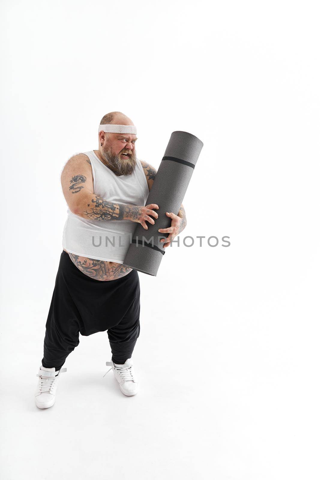 Happy fat man with big belly and tattos in sports wear with exercise mat
