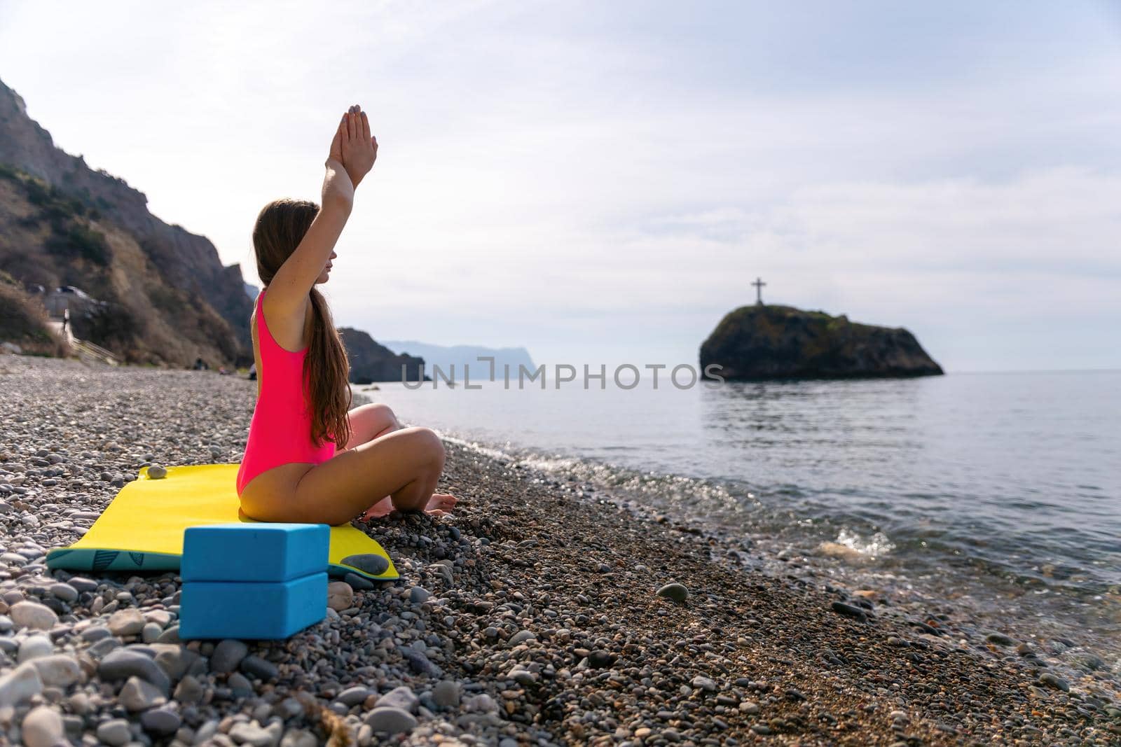 Young beautiful caucasian woman with long hair in pink swimsuit practicing fitess, pilates and modern yoga on the beach at sunrise near the sea. Healthy lifestyle. Meditation concept. Selective focus by panophotograph