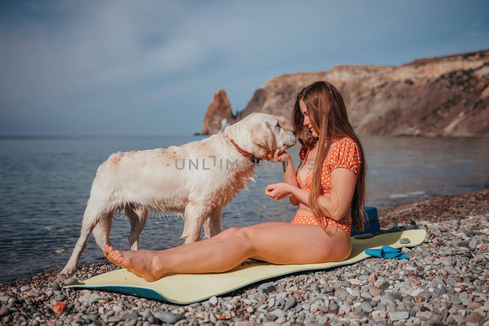 Young woman in swimsuit with long hair practicing stretching outdoors on yoga mat by the sea on a sunny day. Women's yoga fitness pilates routine. Healthy lifestyle, harmony and meditation concept.