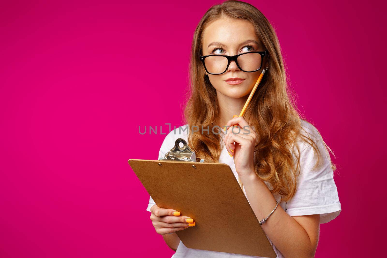 Young beautiful smiling woman standing and holding clipboard against pink background