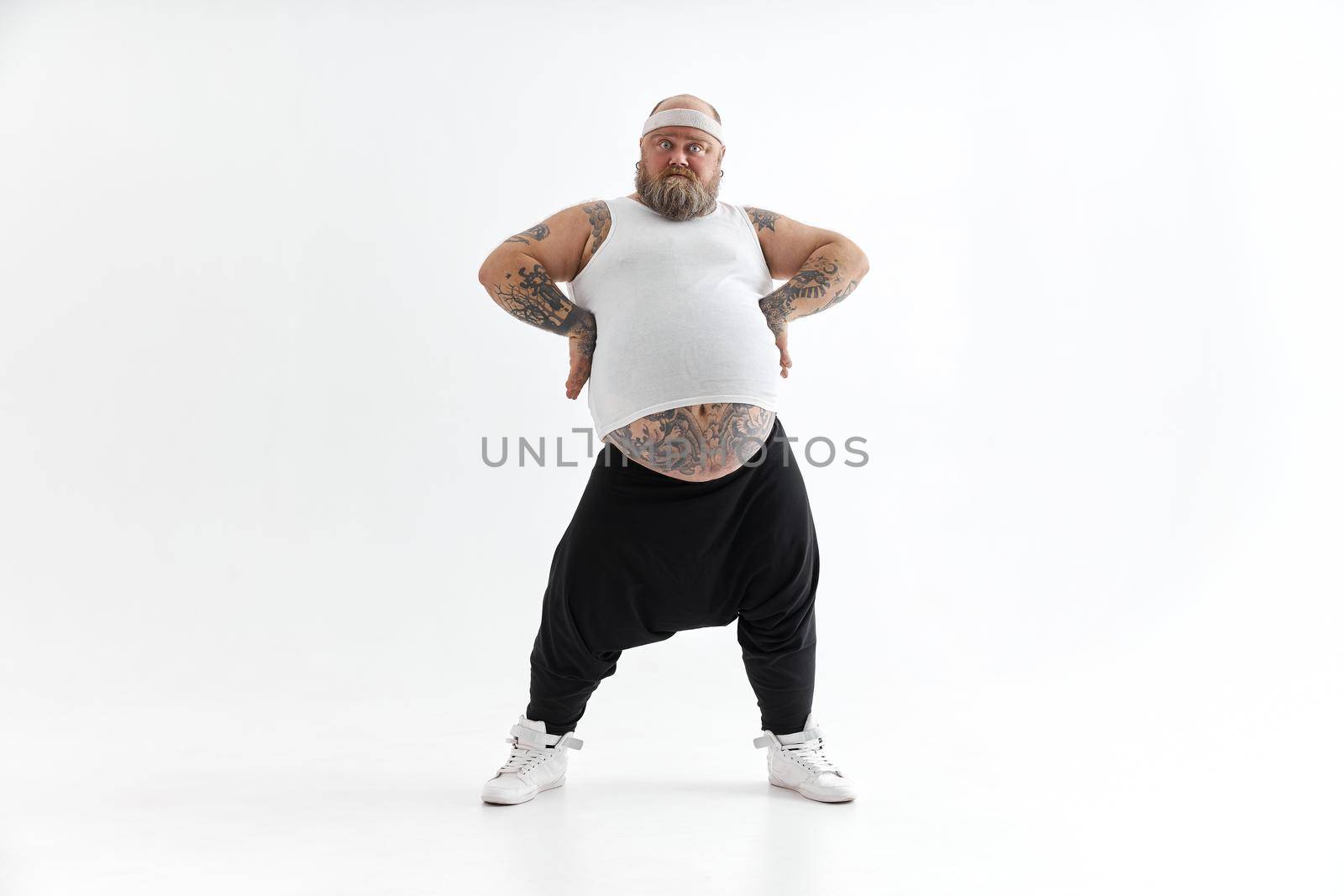 Happy fat man with big belly and tattoes in sports wear posing on white background
