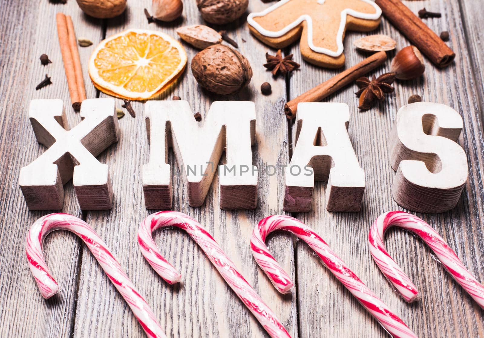 Gingerbreads with spices on the wooden table, wooden letters XMAS and Santa staffs candies. Christmas aroma decor