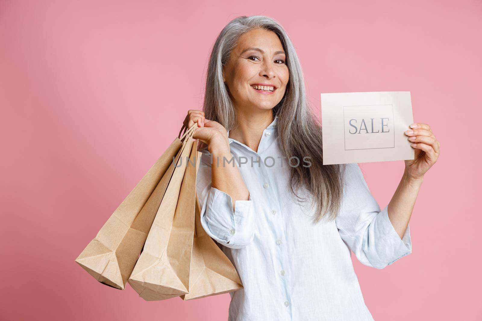 Beautiful middle aged lady holds paper shopping bags and card with word Sale in studio by Yaroslav_astakhov