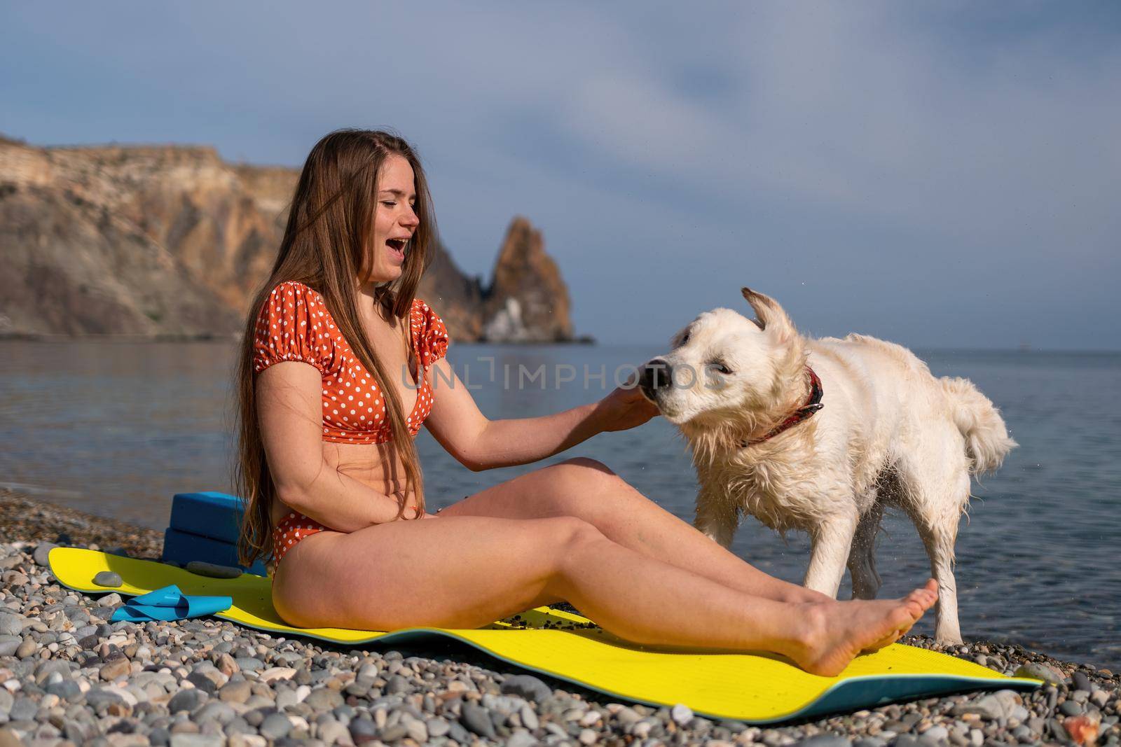 Young woman in swimsuit with long hair practicing stretching outdoors on yoga mat by the sea on a sunny day. Women's yoga fitness pilates routine. Healthy lifestyle, harmony and meditation concept.