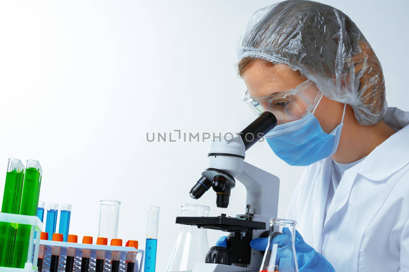 Woman scientist looking through a microscope in laboratory by Fabrikasimf