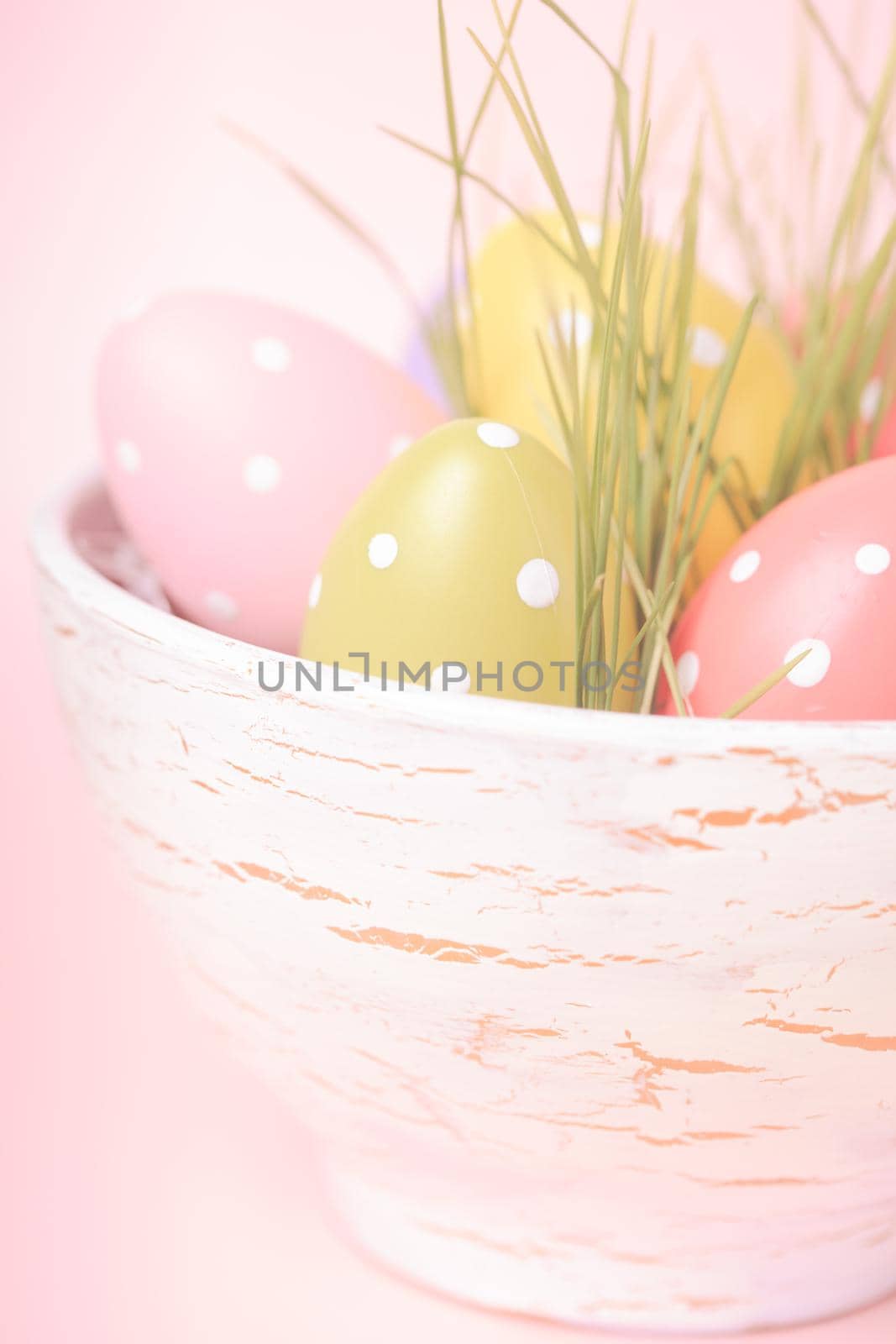 Decorative eggs in pot with grass over pink background. Easter decor.