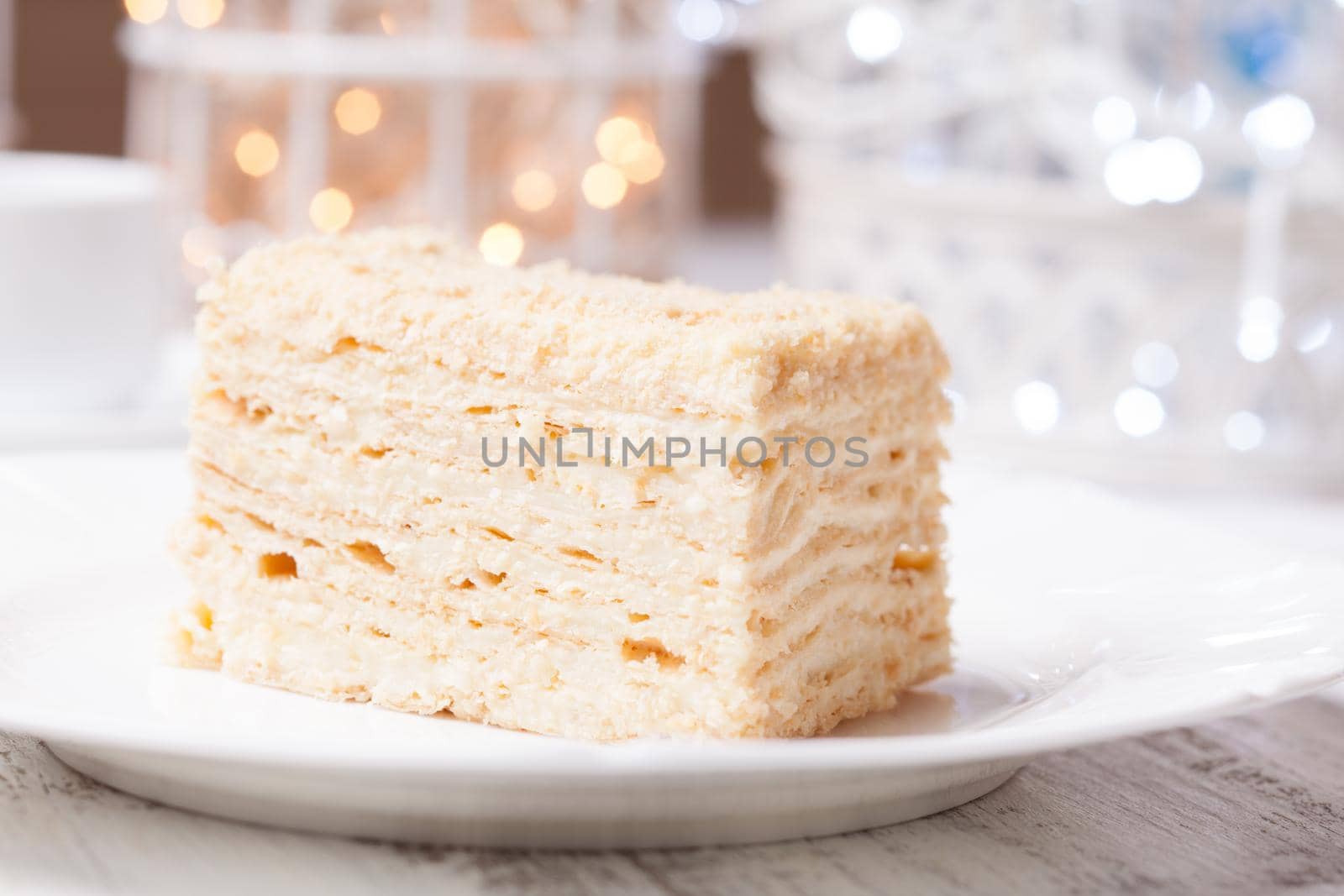 Piece of napoleon cake on a plate, over defocused light background