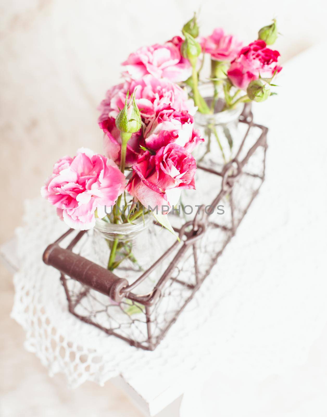 Pink flowers in glass bottles in metal basket. Vintage decor concept