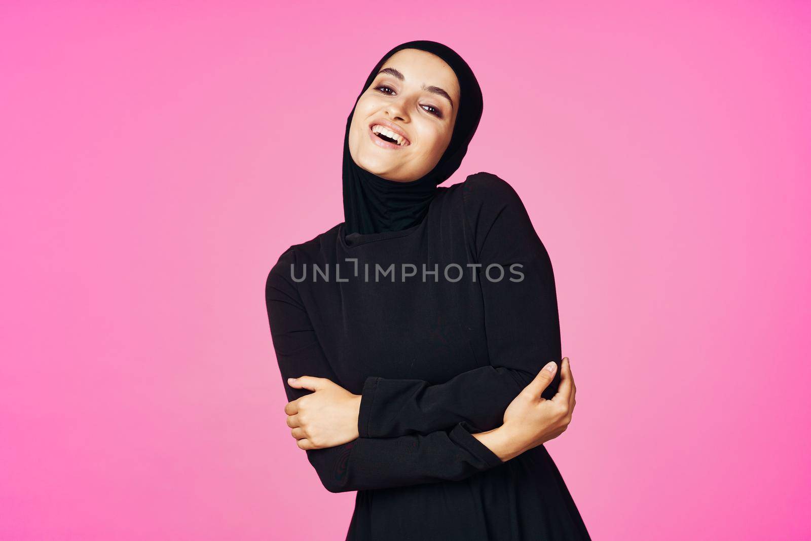 cheerful muslim woman in black hijab posing fashion pink background. High quality photo