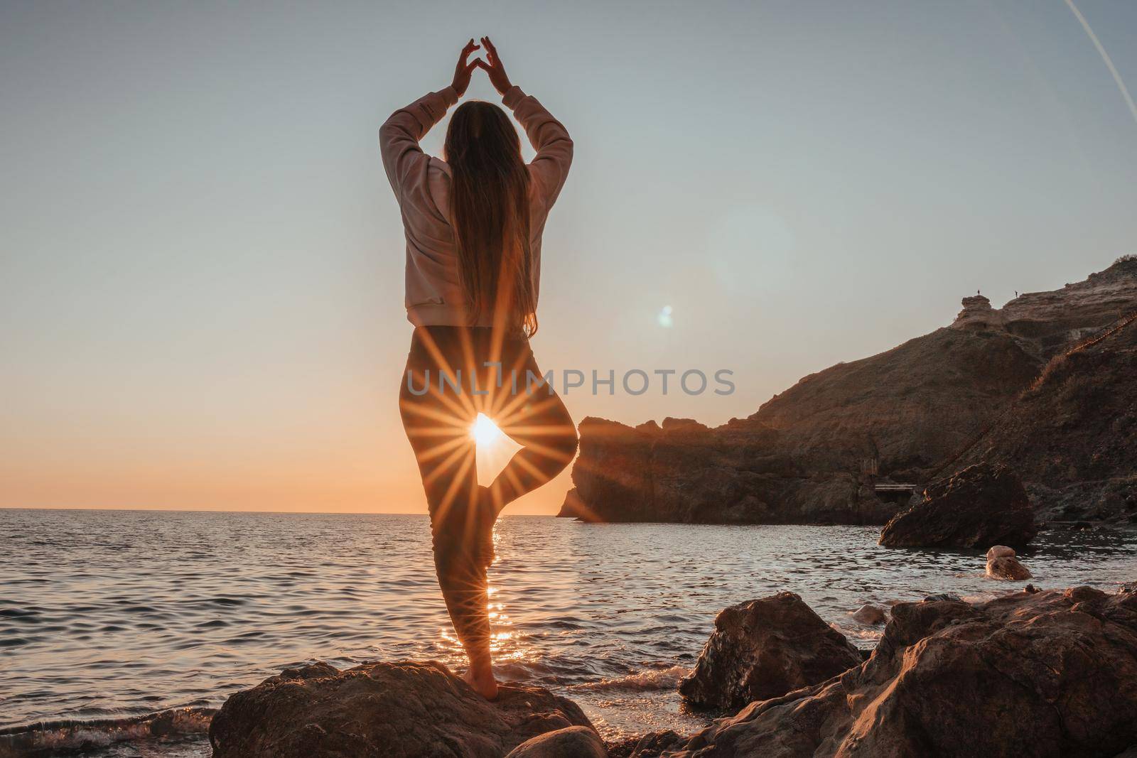 Young woman in swimsuit with long hair practicing stretching outdoors on yoga mat by the sea on a sunny day. Women's yoga fitness pilates routine. Healthy lifestyle, harmony and meditation concept.