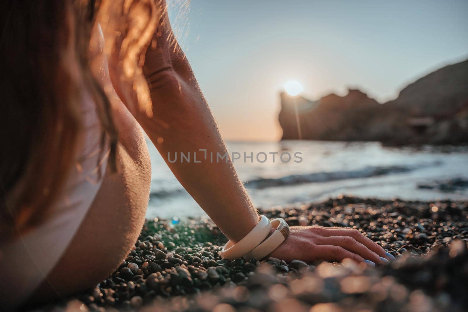 Young woman with long hair in white swimsuit and boho style braclets practicing outdoors on yoga mat by the sea on a sunset. Women's yoga fitness routine. Healthy lifestyle, harmony and meditation by panophotograph