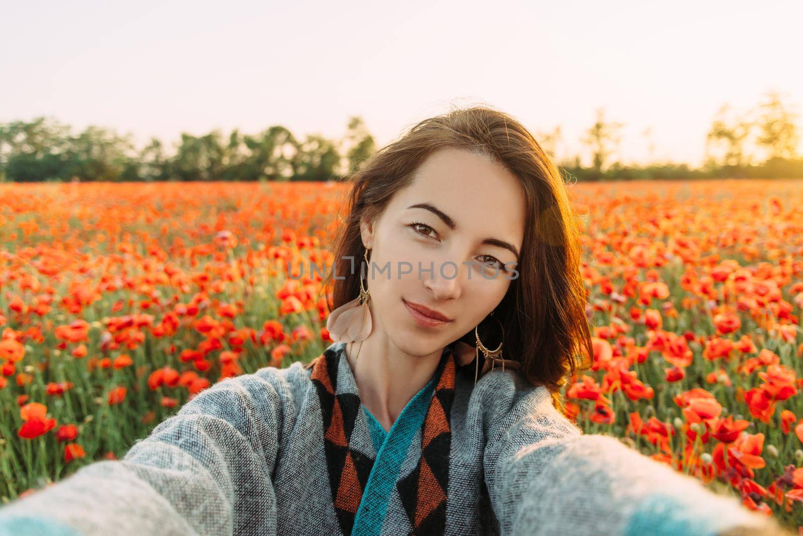 Point of view image of smiling beautiful young woman taking photo selfie in poppy flower field in summer.