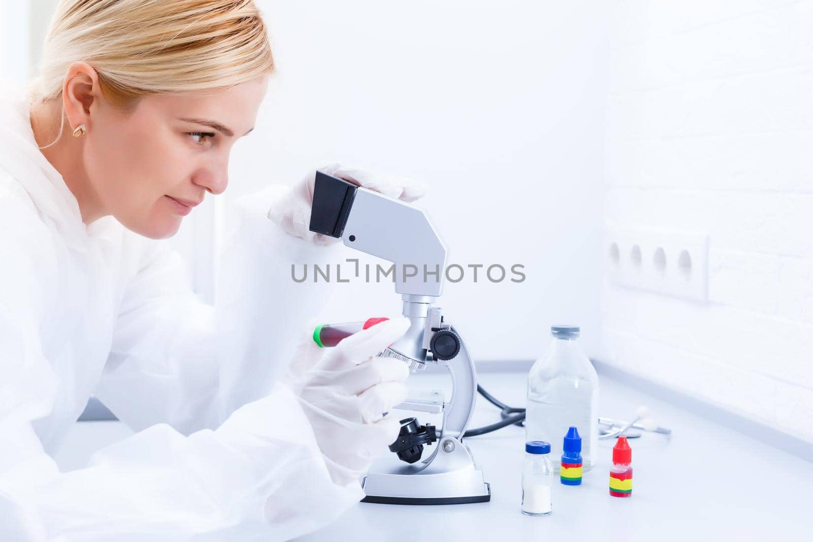 A beautiful female medical or scientific researcher using her microscope in a laboratory. by Andelov13