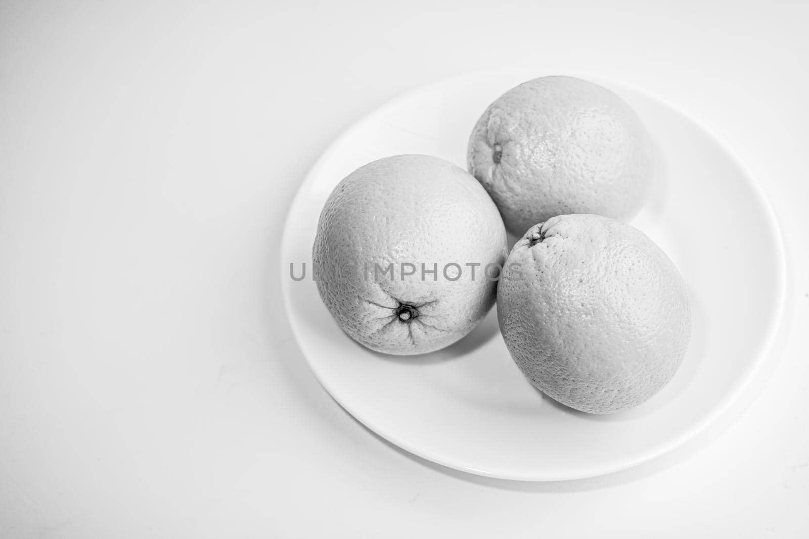 Three oranges in a plate on a white background. Black and white photo. Still life. Selective focus.