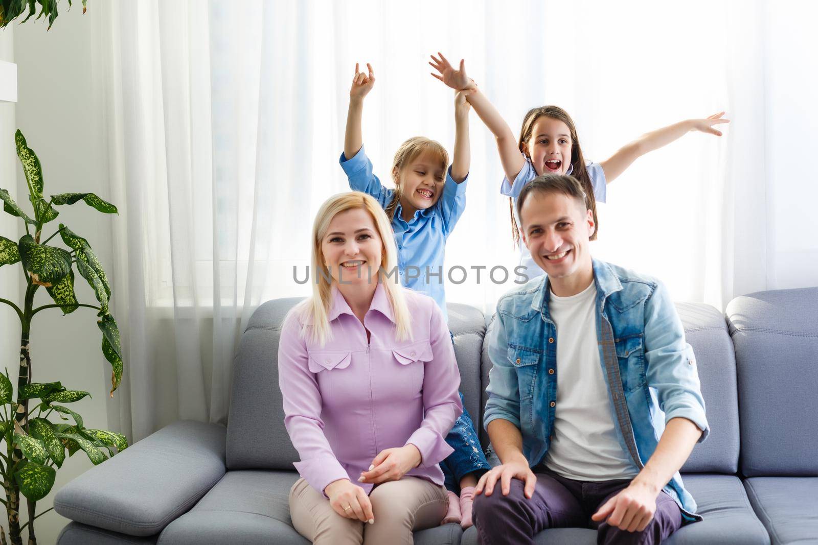 Cheerful young family with kids laughing sitting on couch together, parents with children enjoying entertaining at home by Andelov13