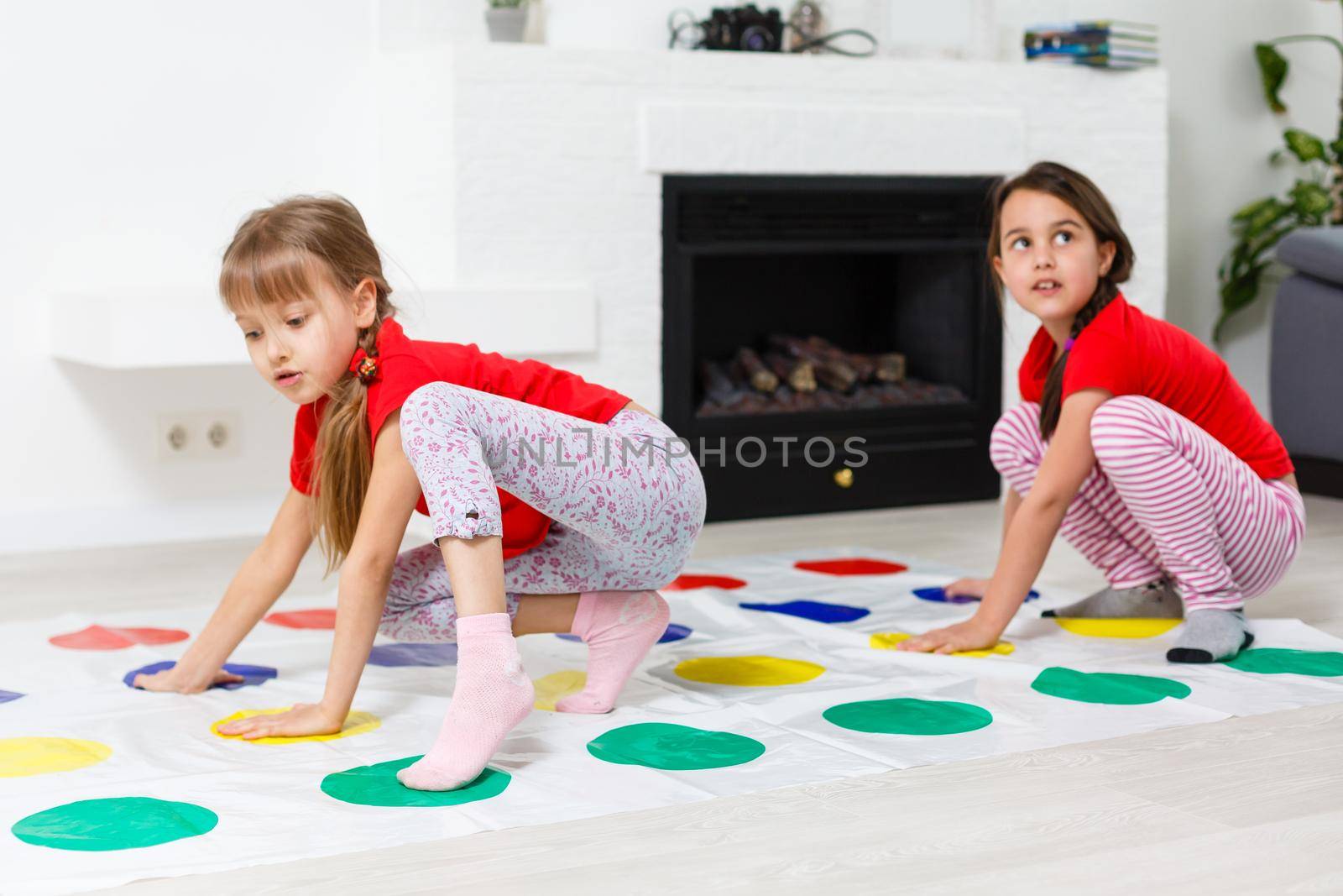 Two happy girls in children's clothes enthusiastically play on the floor.