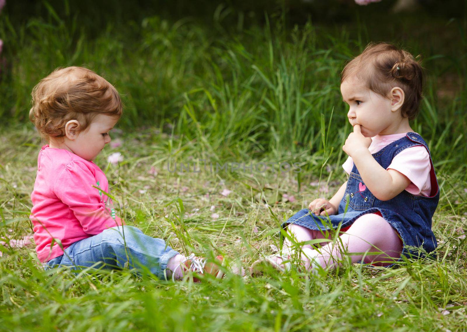 Two girls play in the garden, sitting on the grass