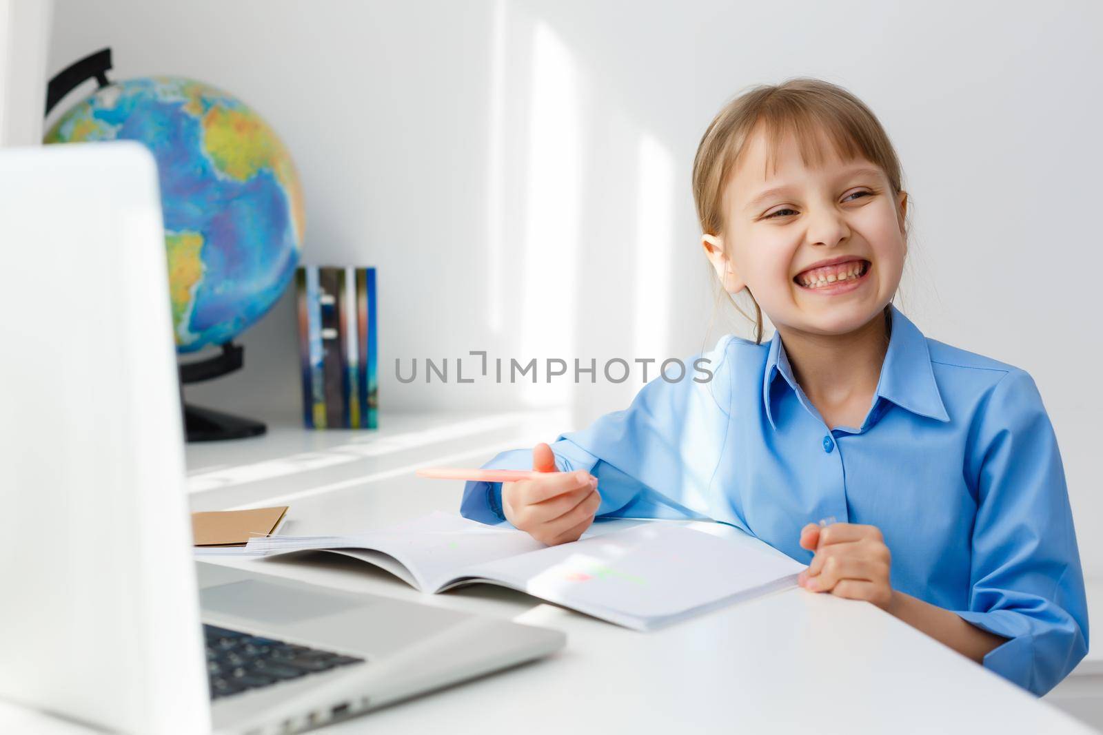 Cute little girl is sitting at table with her laptop and studying online