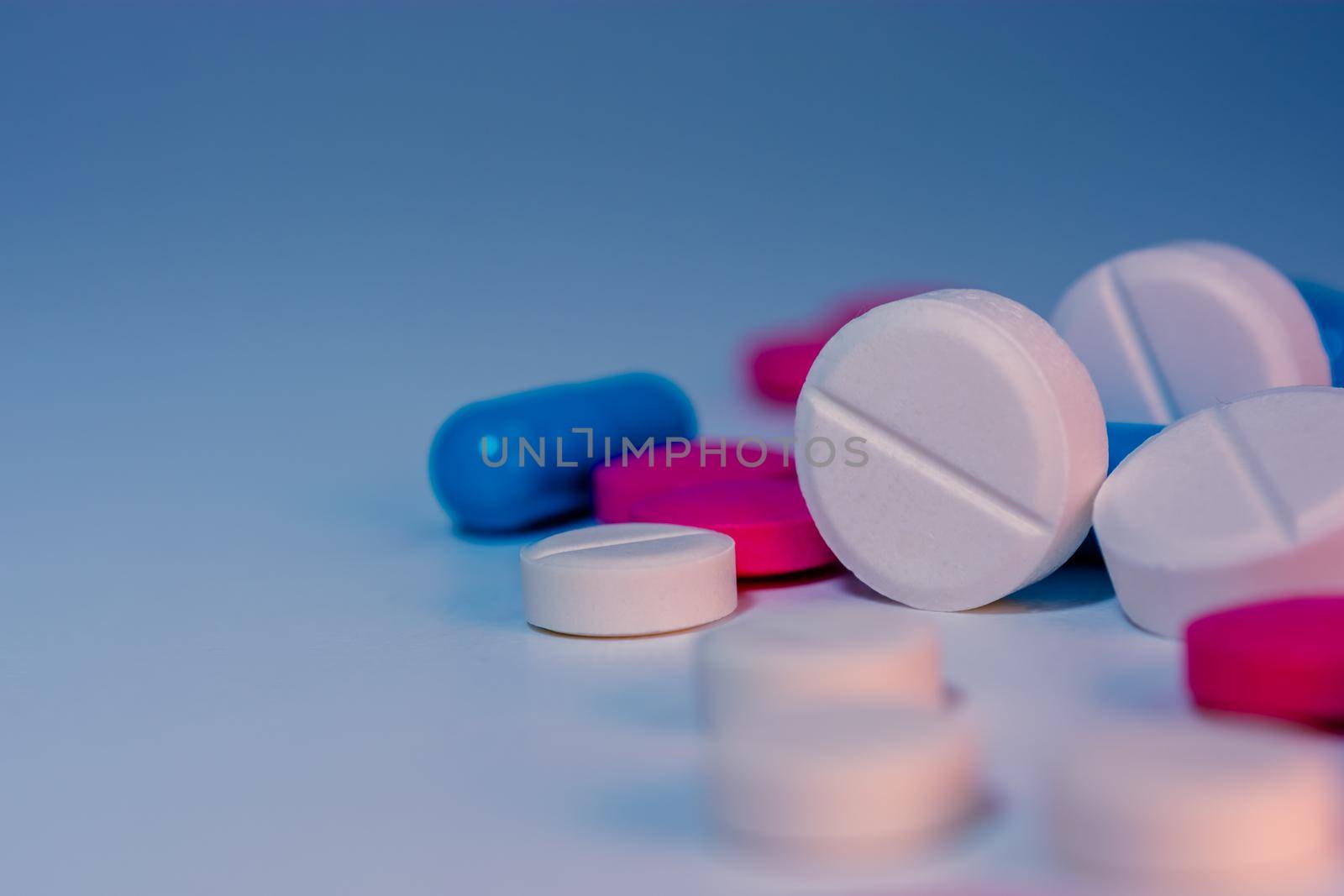 Several scattered pills on the table close-up on a colorful background. Medical theme. Selective focus.