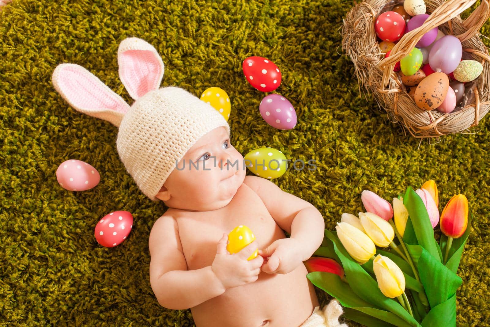 Three months baby lying on on the grass carpet as a Easter bunny