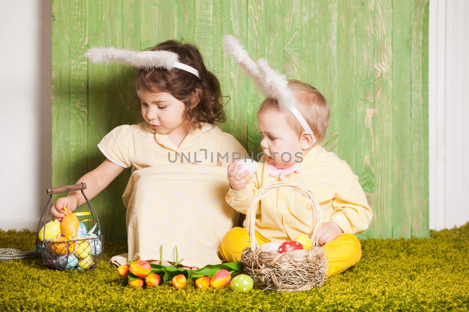 Little boy and girl as a Easter rabbits on the grass with colorful eggs