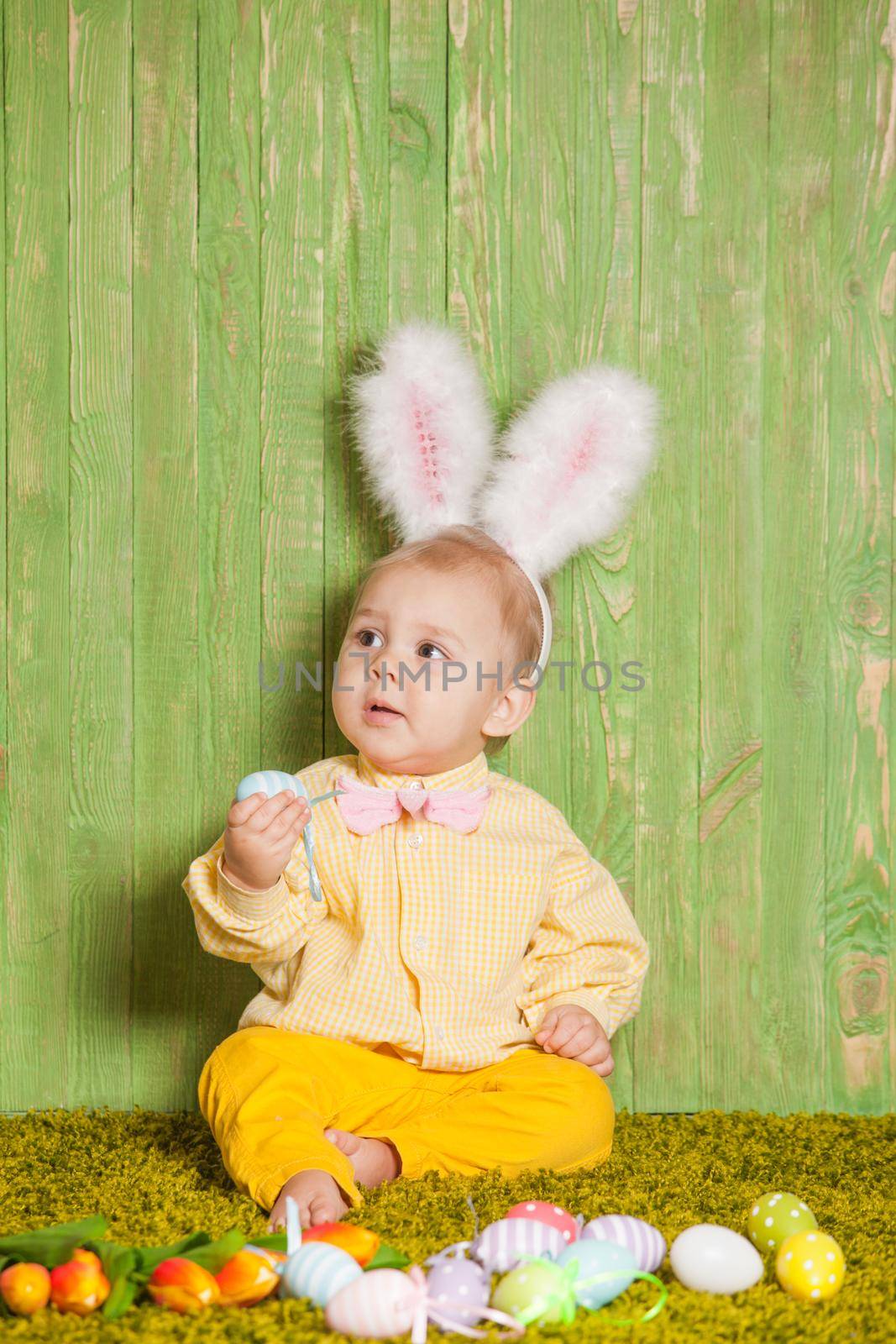 Little boy as a Easter rabbit on the grass with colorful eggs