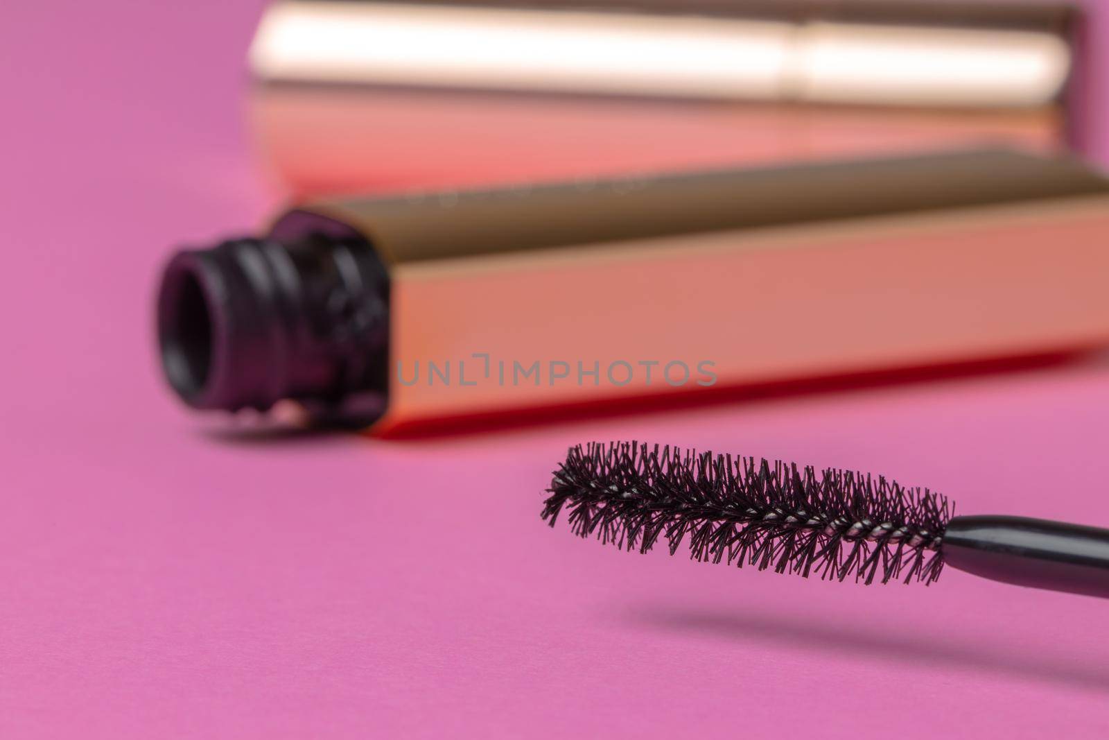 Open gold tube of mascara close up on pink background