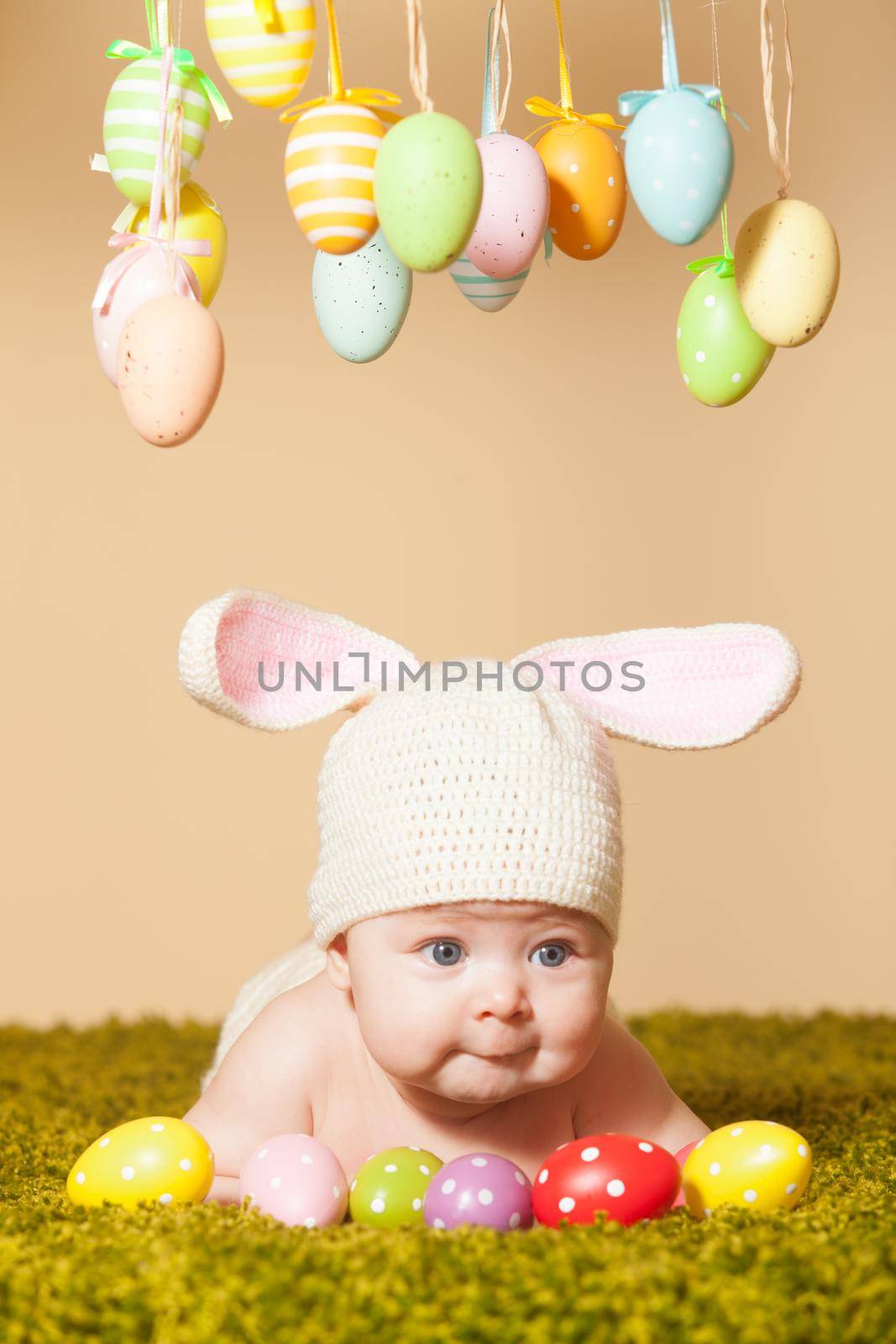 Three months baby lying on his stomach as a Easter bunny on the grass with eggs
