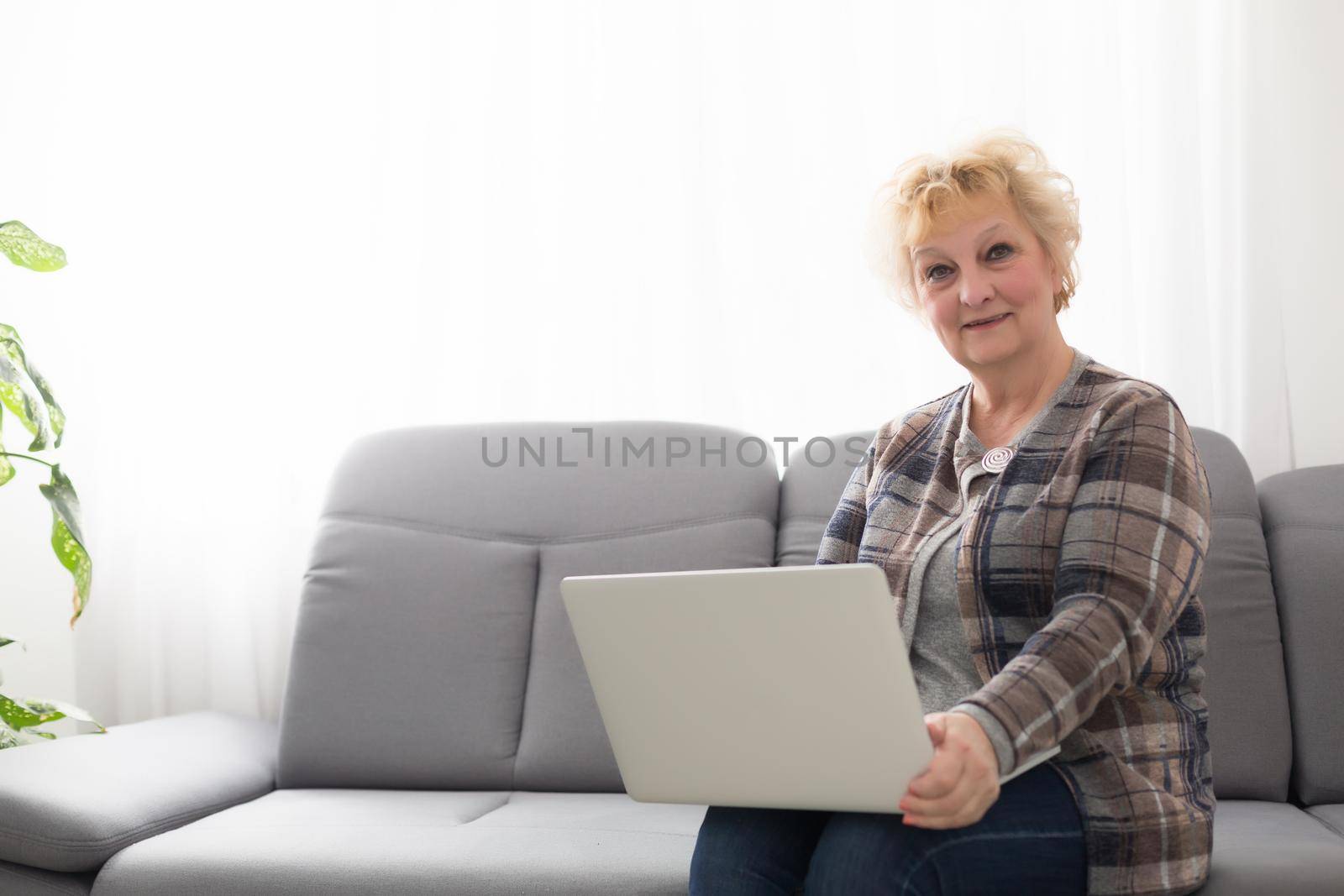Elderly woman sitting at home, using laptop computer, smiling. by Andelov13
