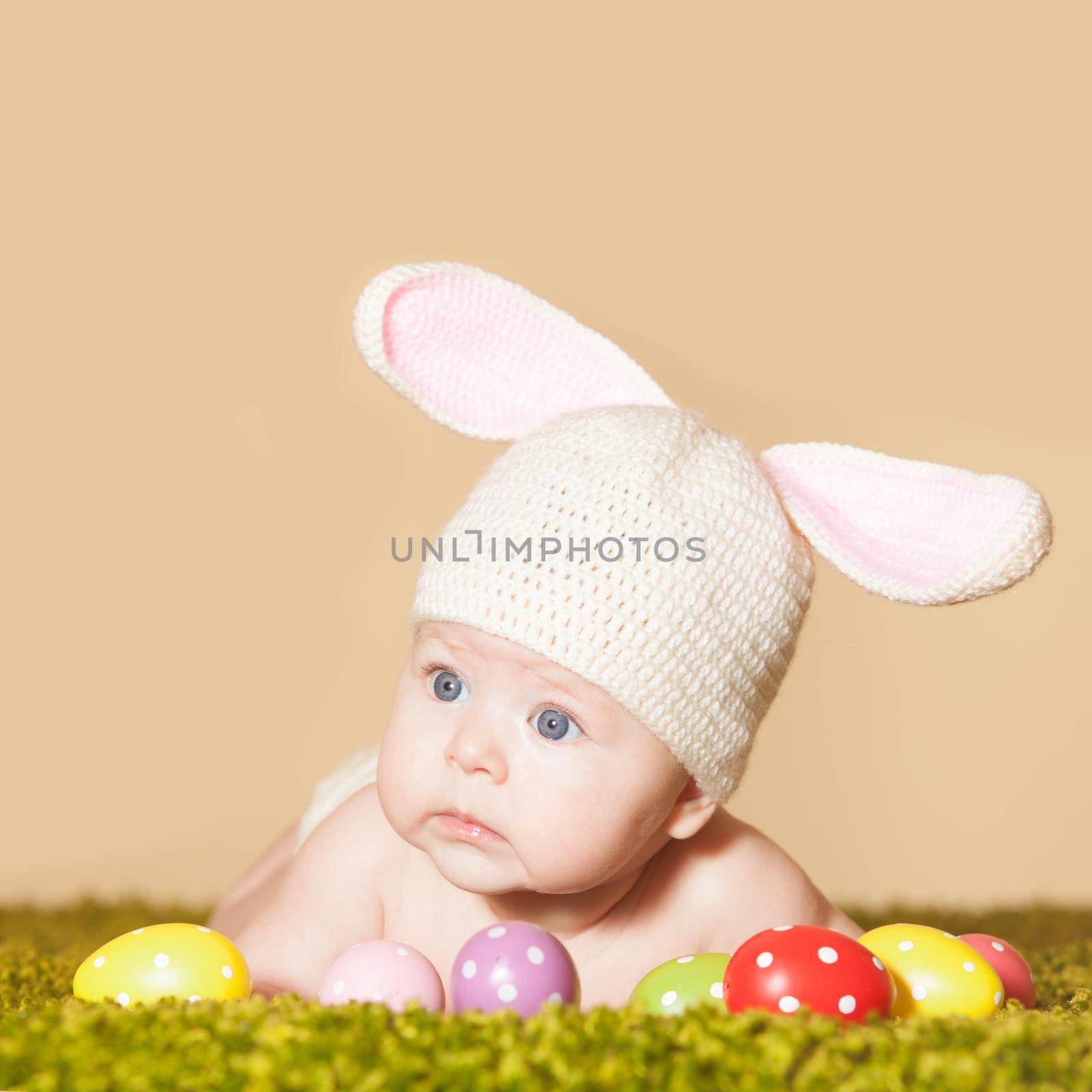 Three months baby lying on his stomach as a Easter bunny on the grass with eggs