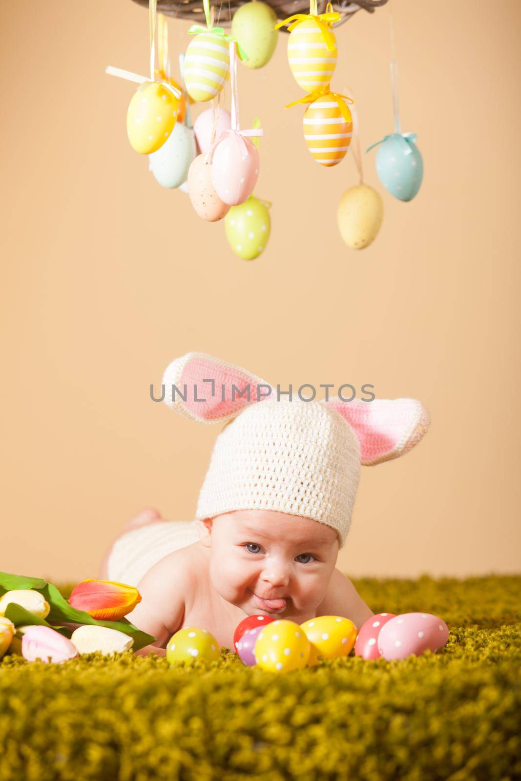 Three months baby lying on his stomach as a Easter bunny on the grass with eggs