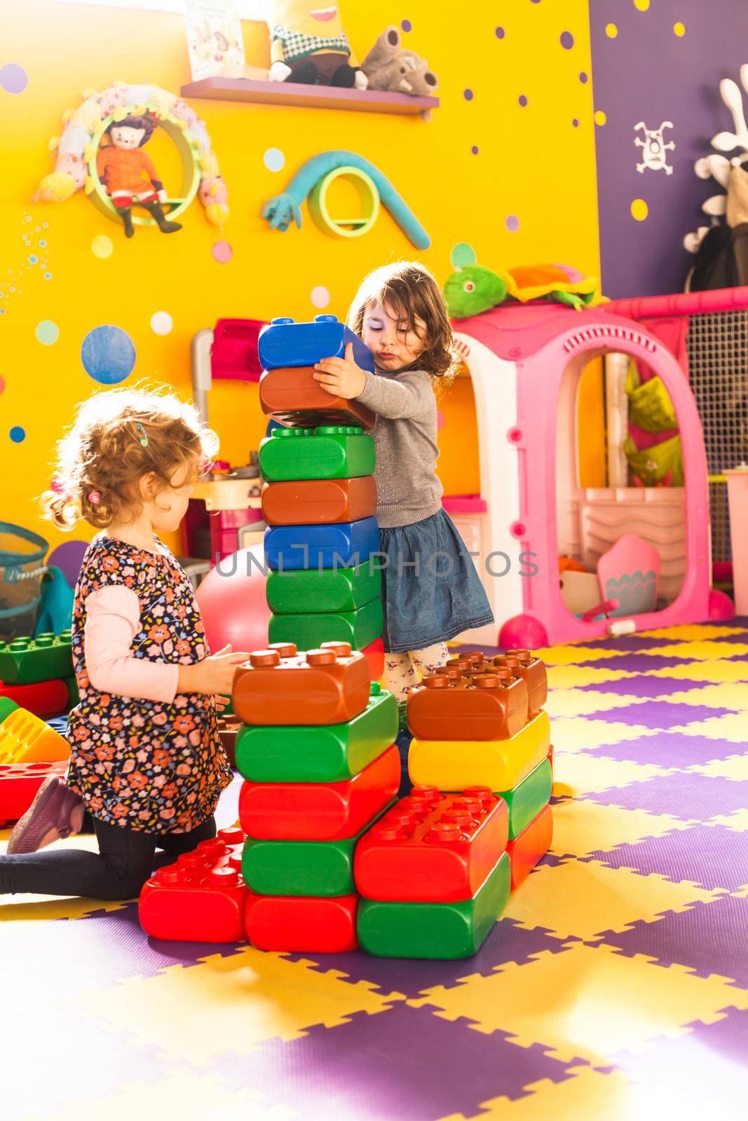 Two girls play with big bricks in playroom