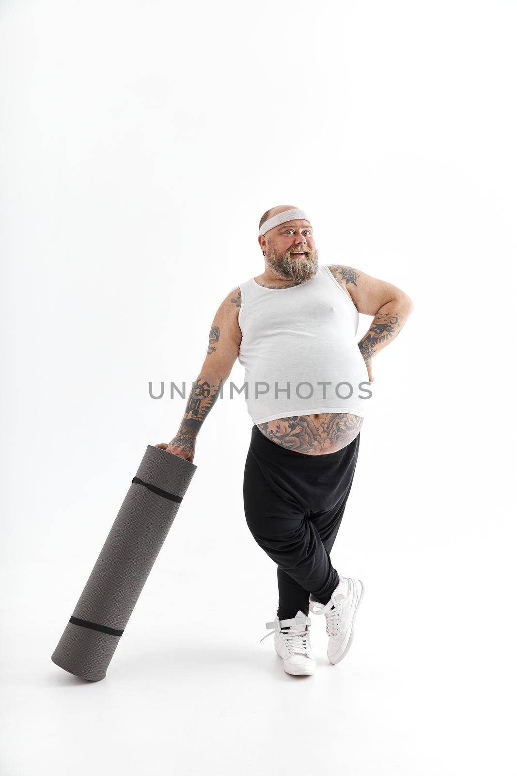 Happy fat man with big belly and tattos in sports wear with exercise mat