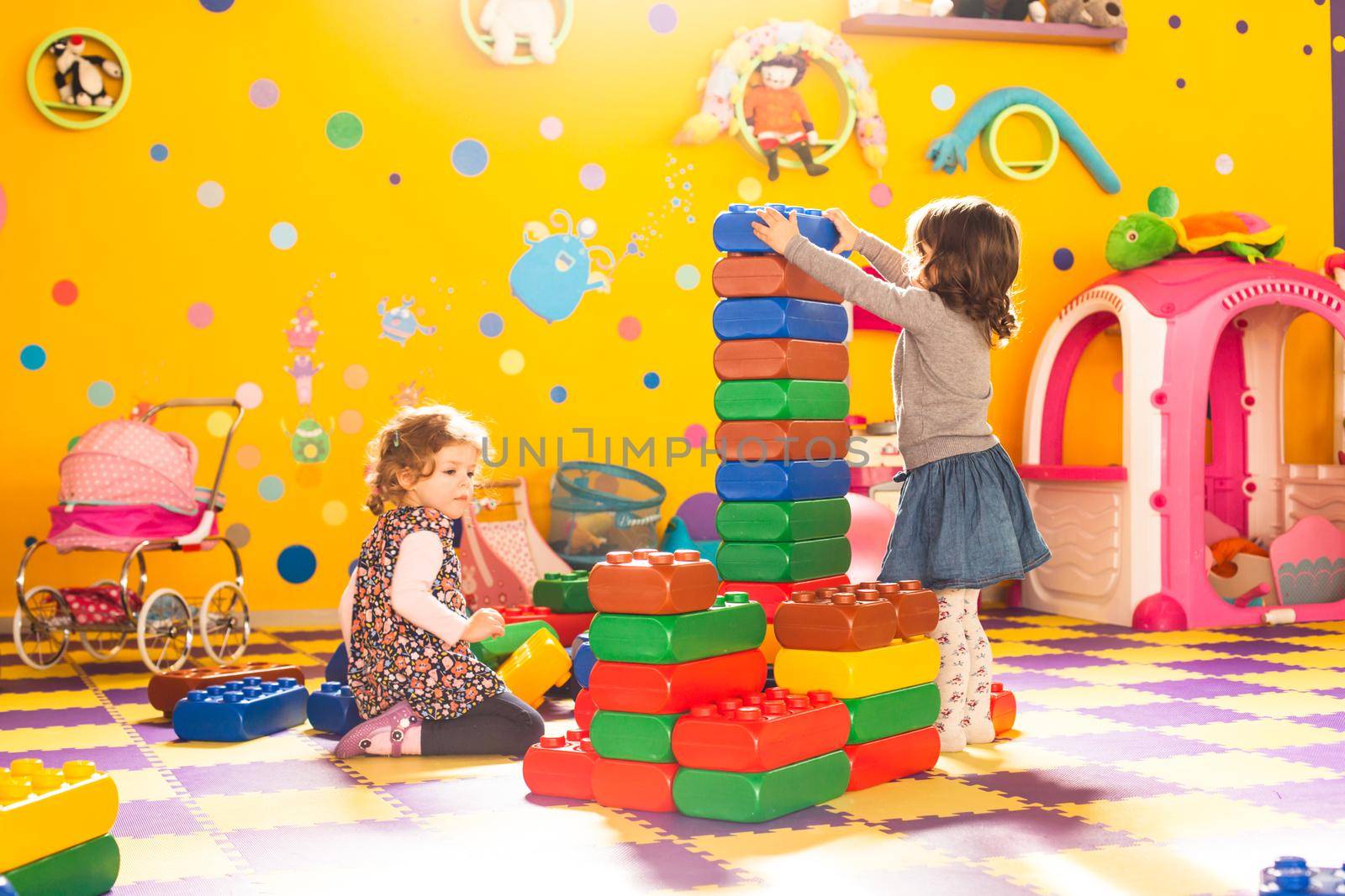 Two girls play with big bricks in playroom