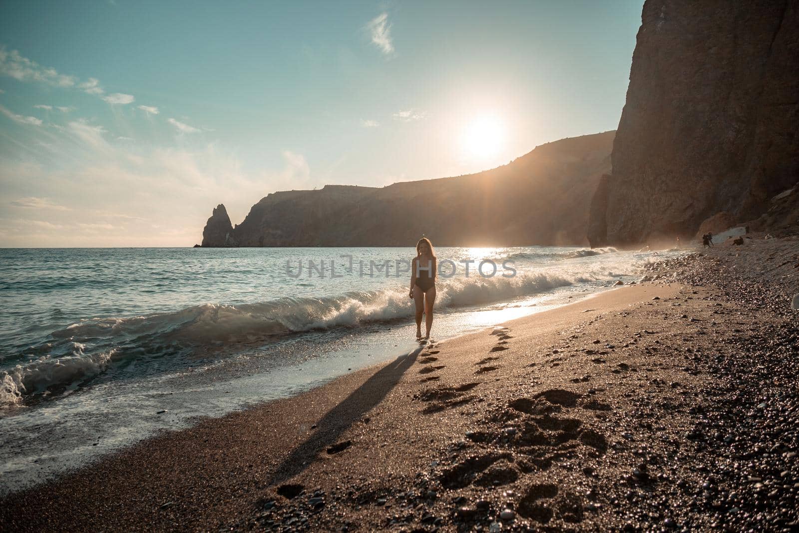 Selective focus. Happy carefree sensual woman with long hair in black swimwear posing at sunset beach. Silhouette of young beautiful playful positive woman outdoor. Summer vacation and trip concept.
