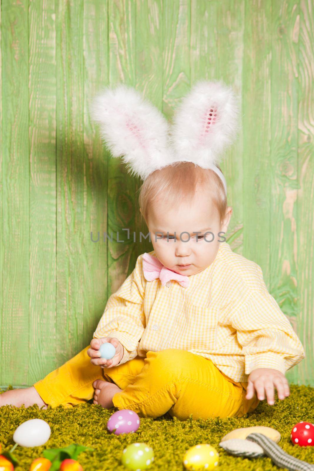 Little boy as a Easter rabbit on the grass is hunting for colorful eggs