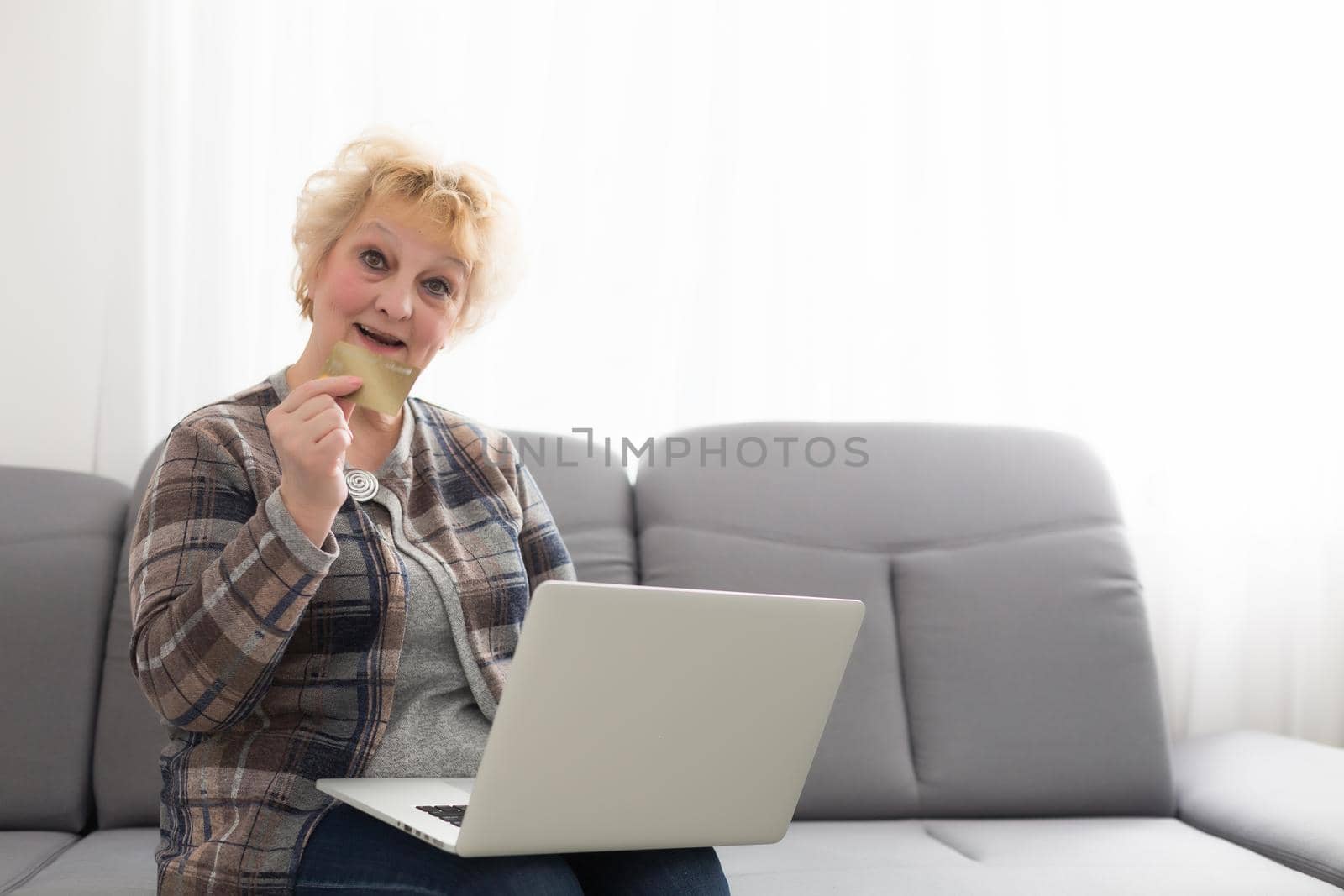Old woman holding a credit card in front of laptop with blank screen