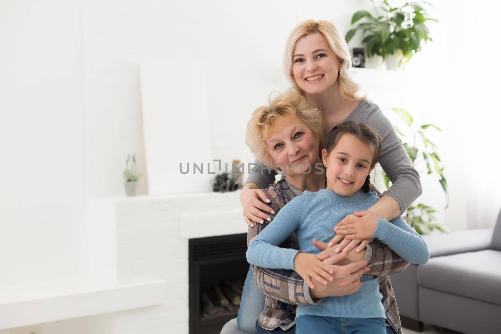 Three generations of women. Beautiful woman and teenage girl are kissing their granny while sitting on couch at home